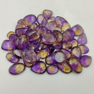 May include: A pile of purple and yellow gemstone cabochons, cut in a teardrop shape. The stones are translucent and have a slight shimmer.