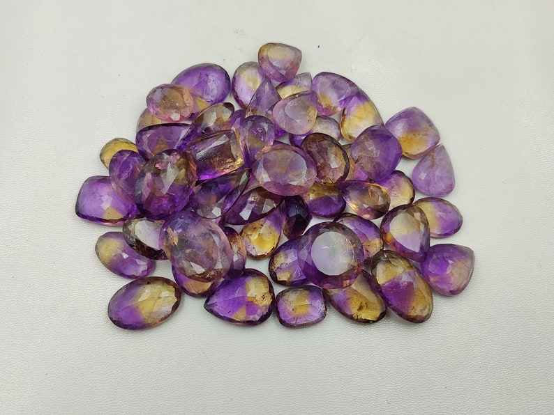 May include: A pile of purple and yellow gemstone cabochons, cut in a teardrop shape. The stones are translucent and have a slight shimmer.