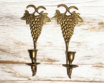 May include: A pair of brass wall sconces with a grapevine design. Each sconce has a candle holder and a grape cluster.