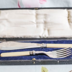 Puede incluir: Un juego vintage de cuchillo y tenedor de mantequilla de plata con mangos de marfil, en una caja forrada de terciopelo negro.