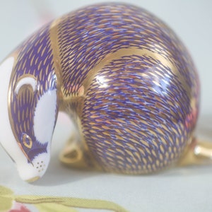 Peut inclure: Une petite figurine en porcelaine d'un blaireau, peinte dans des tons de violet et d'or. Le blaireau est enroulé dans une position de sommeil.