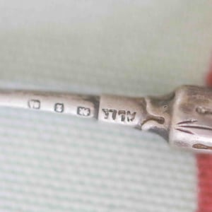 May include: A silver hook with a pearl handle. The hook is marked with the letters "WLL" and three small squares.
