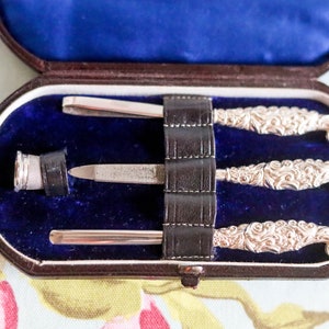 Puede incluir: Un juego de manicura vintage de plata en un estuche forrado de terciopelo azul. El juego incluye una lima de u&ntilde;as, unas pinzas y dos empujadores de cut&iacute;culas.