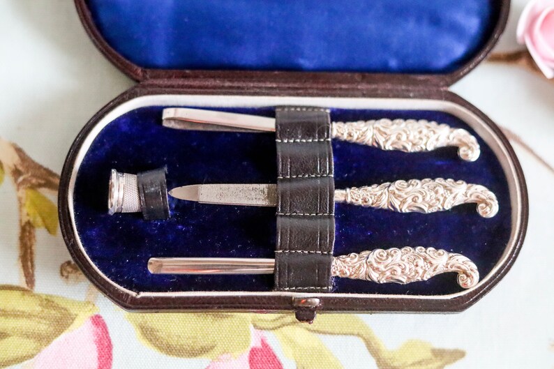 Puede incluir: Un juego de manicura vintage de plata en un estuche forrado de terciopelo azul. El juego incluye una lima de u&ntilde;as, unas pinzas y dos empujadores de cut&iacute;culas.