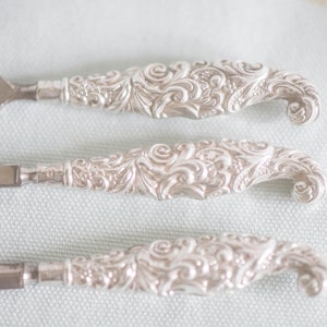 Puede incluir: Tres limas de u&ntilde;as de plata con dise&ntilde;os florales ornamentados. Las limas tienen un extremo puntiagudo y un mango redondeado.