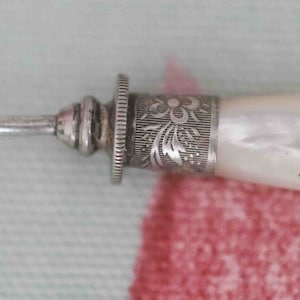 May include: A silver and white mother-of-pearl thimble with a decorative floral design.