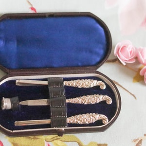Puede incluir: Un juego de manicura vintage de plata con tres herramientas en un estuche de terciopelo marr&oacute;n y azul.
