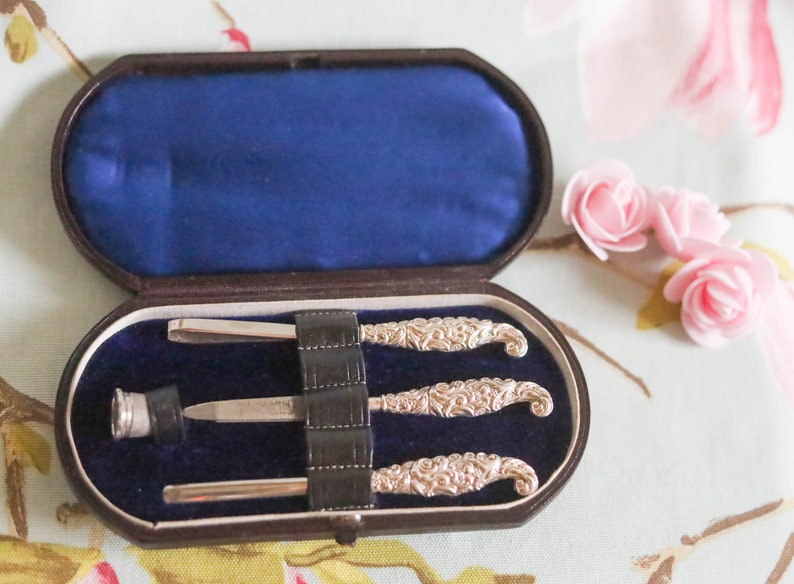Puede incluir: Un juego de manicura vintage de plata con tres herramientas en un estuche de terciopelo marr&oacute;n y azul.