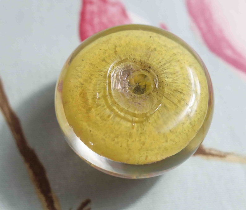 May include: A round, yellow glass bead with a clear center and a textured surface.