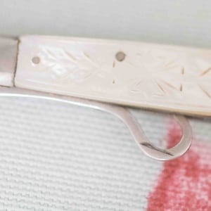 May include: A small, white, pearl-handled pocket knife with a silver blade. The handle has a delicate floral design.