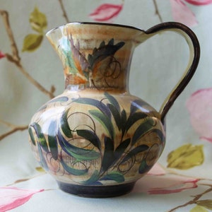 May include: A cream-coloured ceramic jug with a brown handle and a floral design in shades of green, blue, and brown.
