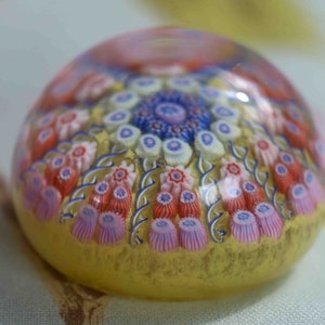 May include: A glass paperweight with a colorful floral design. The paperweight is round and has a clear glass base. The flowers are in shades of pink, blue, and white.