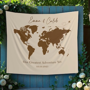 May include: A beige fabric backdrop with a brown world map and the text "Emma & Caleb" and "Our Greatest Adventure Yet 03.03.2025".
