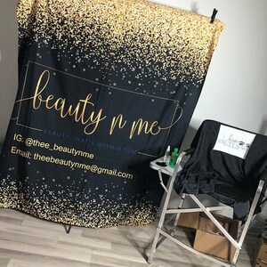 May include: Black backdrop with gold glitter and the text "beauty n me - BEAUTY THAT'S WITHIN YOU" with contact information below. A black makeup chair with a white logo that says "beauty n me" is in the foreground.