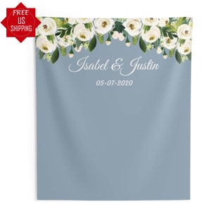 May include: A light blue backdrop with a white floral garland at the top. The text "Isabel & Justin" and the date "05-07-2020" are printed in white below the garland.