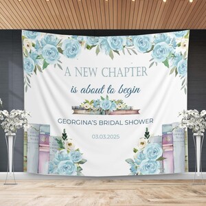 Peut inclure: Une toile de fond blanche avec le texte "A NEW CHAPTER is about to begin" et "GEORGINA'S BRIDAL SHOWER 03.03.2025". Le design comprend des roses bleu clair et des piles de livres. Des compositions florales encadrent le texte.