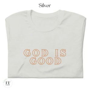 Op de afbeelding: Een wit T-shirt met de tekst "GOD IS GOOD" in oranje.