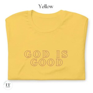 Op de afbeelding: Geel T-shirt met de tekst "GOD IS GOOD" gedrukt in een bruine omtrek.