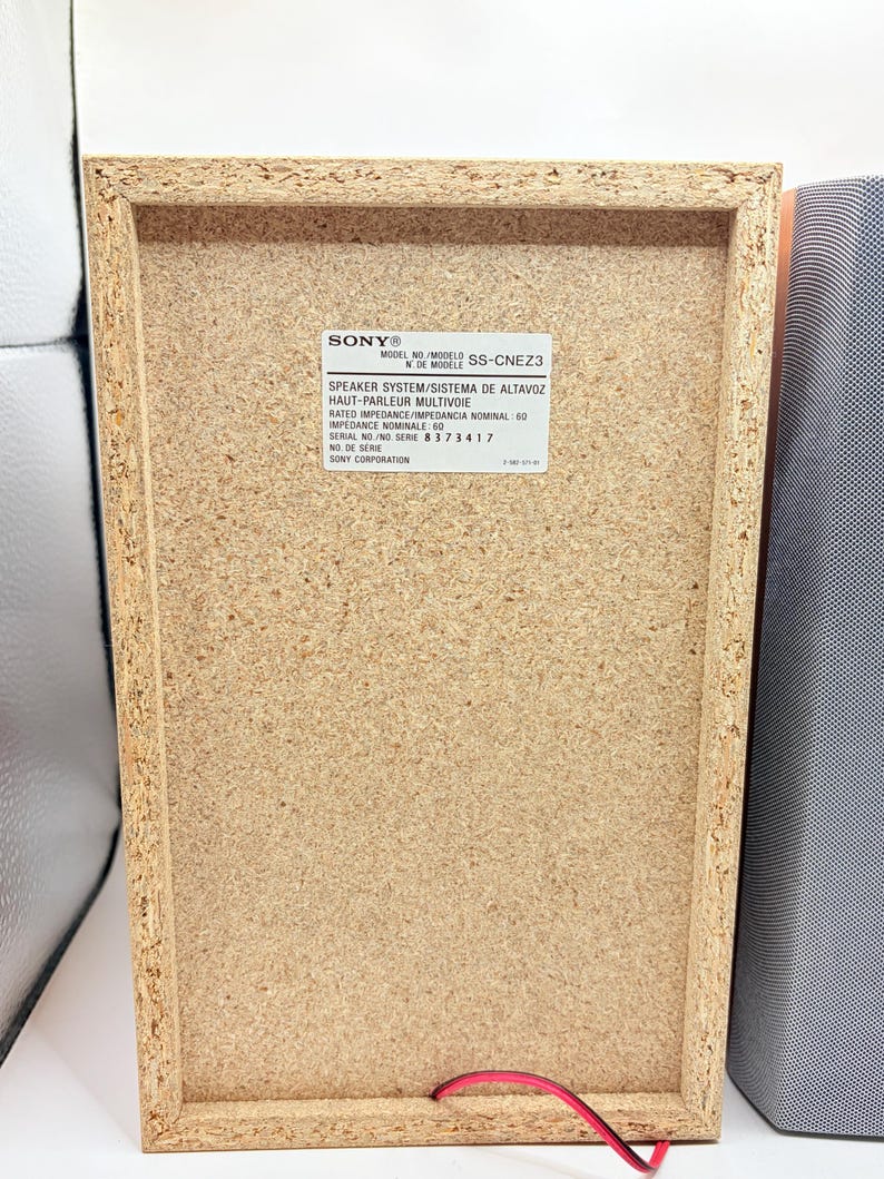 May include: The back panel of a rectangular Sony speaker system, model SS-CNEZ3, featuring a light brown particle board finish. A white label displays technical specifications including rated impedance of 6 ohms and serial number 8 373 417.