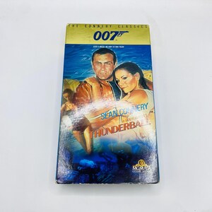 May include: VHS tape for the movie "Thunderball" starring Sean Connery. The cover features a blue and yellow background with images of the actors. The text "The Connery Classics" and "007" are at the top.