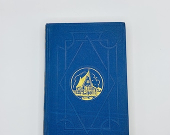 May include: A blue hardcover book with a gold design on the front cover. The design features a house with a pointed roof and a chimney, surrounded by a circle and a diamond shape.