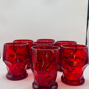 May include: Set of six vintage red drinking glasses. Each glass has a unique, textured design and a flared base. The glasses are made of a deep red glass and are arranged in a group, showcasing their vibrant color and design.