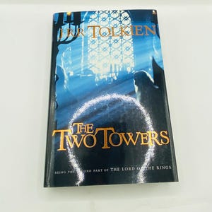 May include: A copy of "The Two Towers" by J.R.R. Tolkien, the second part of "The Lord of the Rings." The book cover features a blue and white illustration with gold lettering. The title is prominently displayed.