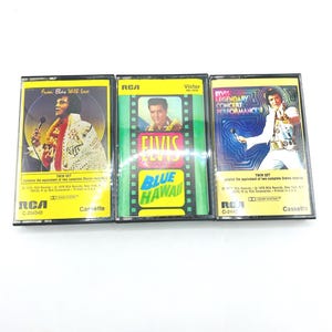 Pode incluir: Três cassetes vintage de Elvis Presley. As cassetes apresentam arte de álbuns com Elvis em várias poses, incluindo uma com o texto "Blue Hawaii". O logótipo da RCA é visível em cada cassete.