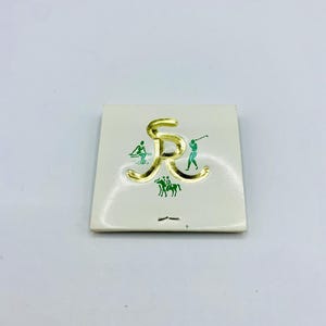 May include: A square, off-white card with a gold-colored letter "R" and green illustrations of people playing golf and riding horses. The card has a gold border and is set against a white background.