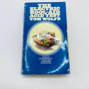May include: A vintage paperback book titled "The Electric Kool-Aid Acid Test" by Tom Wolfe. The book has a blue cover with white and yellow text. The cover features a colorful illustration within a circular design.