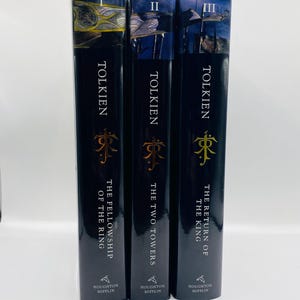 May include: Three hardcover books by Tolkien. The spines are black with gold lettering and a gold emblem. The titles are "The Fellowship of the Ring", "The Two Towers", and "The Return of the King". The publisher is Houghton Mifflin.