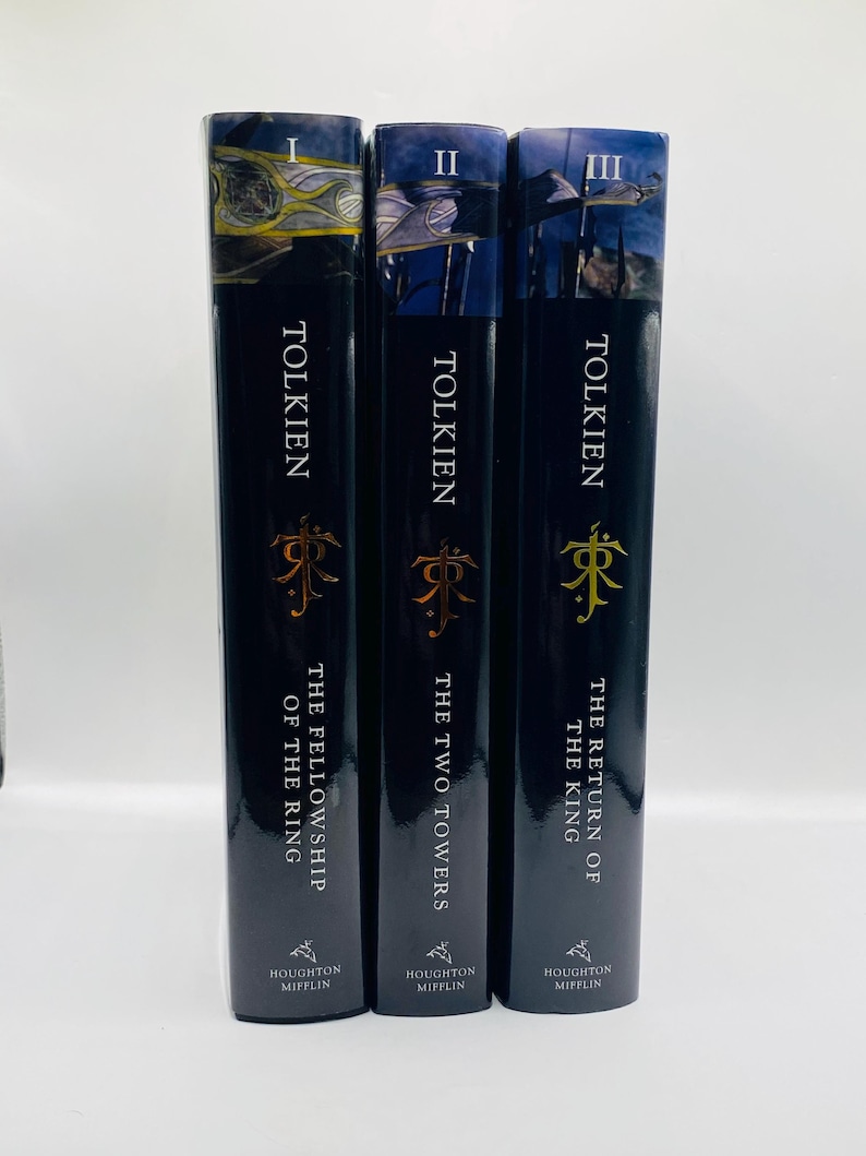 May include: Three hardcover books by Tolkien. The spines are black with gold lettering and a gold emblem. The titles are "The Fellowship of the Ring", "The Two Towers", and "The Return of the King". The publisher is Houghton Mifflin.