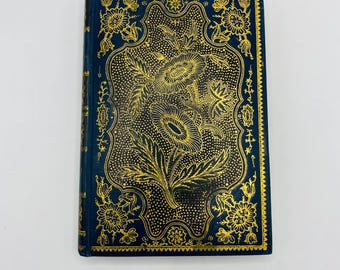 Könnte beinhalten: Ein kleines, dunkelblaues Buch mit einem goldenen Blumendesign auf dem Einband. Der Einband weist ein verziertes, geprägtes Blumenmuster mit komplizierten Details auf. Die Kanten des Buches sind ebenfalls goldfarben, was ein luxuriöses und elegantes Aussehen erzeugt.