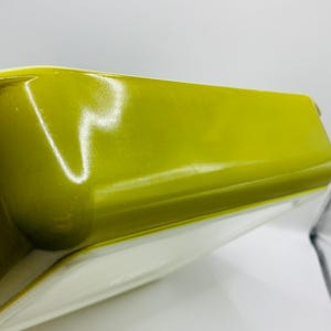 Puede incluir: Un plato para hornear de cerámica verde con un interior blanco. El plato es rectangular y tiene un borde ligeramente redondeado.