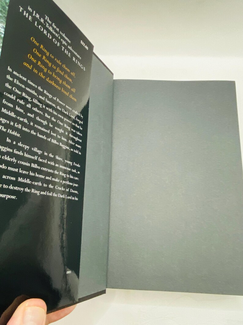 May include: Open book with a black cover featuring the title "The Lord of the Rings" and text from the book. The pages are gray. The book is open to reveal the inside pages.