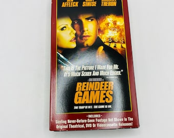 May include: A red VHS tape of the movie "Reindeer Games" featuring Ben Affleck, Gary Sinise, and Charlize Theron. The cover includes the text "Exclusive Director's Cut" and the tagline "The trap is set. The game is on."