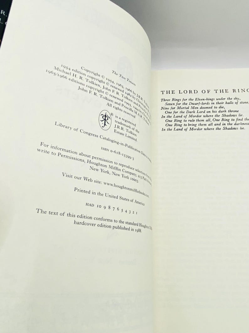 May include: Open book pages with text from "The Lord of the Rings" by J.R.R. Tolkien. The left page shows copyright information, while the right page displays the poem about the rings. The book is printed in the United States.