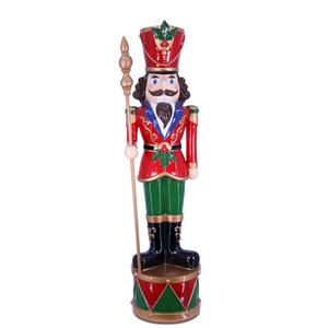 May include: A large, red and green Christmas nutcracker figurine with a gold staff and a drum base. The nutcracker has a black moustache and beard, blue eyes, and a red and white hat with a green holly sprig.