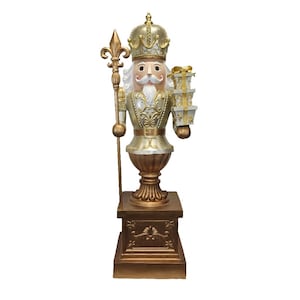 May include: A gold and silver Christmas nutcracker figurine holding a stack of presents. The nutcracker is wearing a crown and holding a staff. The figurine is standing on a gold base.