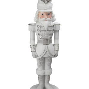 May include: A white Christmas nutcracker figurine with silver detailing. The figurine is dressed in a military-style uniform with a tall hat, a long white beard, and a stern expression. The base is round and decorated with silver scrollwork.