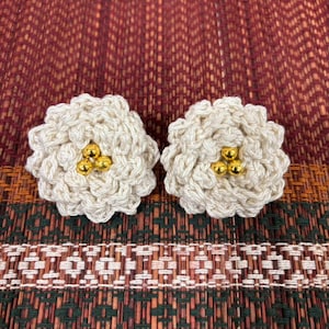 May include: A pair of crocheted flower earrings with gold beads in the center. The earrings are white and have a delicate, feminine design.
