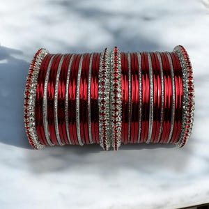 May include: A set of red and silver bangles with rhinestones. The bangles are stacked together and have a shiny finish.