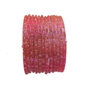 May include: A set of eleven translucent pink bangles arranged in a stack. Each bangle features a faceted, textured surface with small, evenly spaced gold-coloured metallic accents embedded along the outer edge of the circular band.