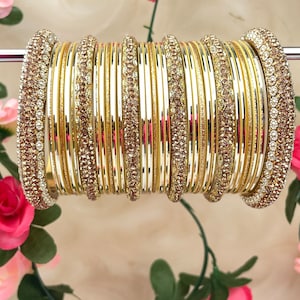 May include: A set of 12 gold bangles with clear and brown rhinestones. The bangles are stacked on a white stand.