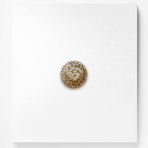 May include: A gold-toned round button with a raised design of clear and gold rhinestones.
