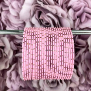 May include: A stack of pink bangles with gold glitter accents. The bangles are arranged in a circle and are on a silver stand.