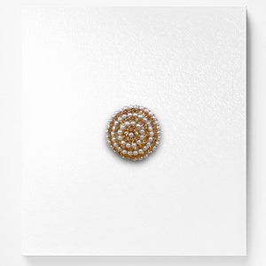 May include: A round, gold-coloured button with a spiral design made of white pearls.