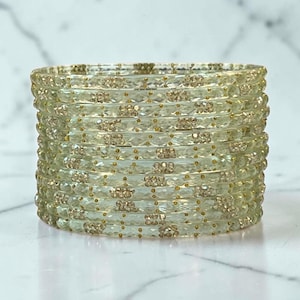 May include: A stack of ten translucent pale yellow bangles featuring a faceted texture and small, evenly spaced gold-coloured metallic dots embedded along the surface of each individual circular bracelet, creating a uniform and repeating pattern.