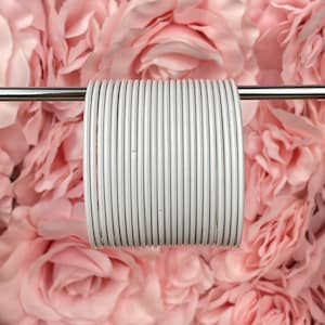 Puede incluir: Un conjunto de brazaletes de metal blanco, dispuestos en círculo, sobre una varilla plateada. Los brazaletes son lisos y brillantes.