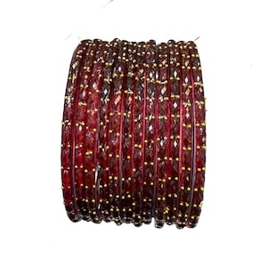 Op de afbeelding: Een set donkerrode armbanden met een gefacetteerd, getextureerd oppervlak en kleine, gelijkmatig verdeelde goudkleurige metalen accenten die langs de buitenrand van elke cirkelvormige armband zijn ingebed, gestapeld tegen een witte achtergrond.
